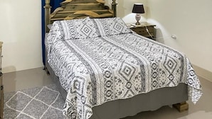 Un dormitorio con cama, mesita de noche, lámpara, ventana con cortinas y un equipo de aire acondicionado.