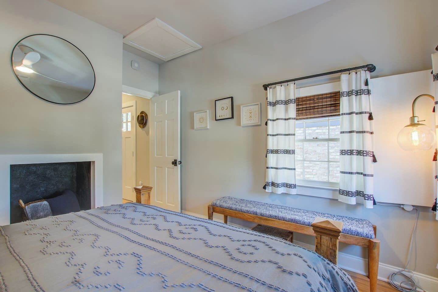 A bedroom with a bed, bedside tables, a mirror, a window with curtains, and a wall-mounted light fixture.