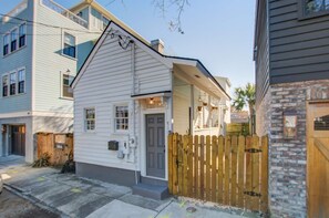 A small, single-story house with a front porch and a wooden fence. - Historic Cottage • walk to King St, fenced yard • patio • hammock • string light (Charleston)