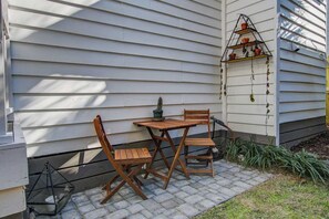 A patio with a wooden table and chairs, a small potted plant, and a metal shelf with potted plants. - Historic Cottage • walk to King St, fenced yard • patio • hammock • string light (Charleston)
