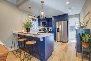 A modern kitchen with a central island, bar stools, a refrigerator, and pendant lighting. - Historic Cottage • walk to King St, fenced yard • patio • hammock • string light (Charleston)
