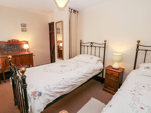 Ein Schlafzimmer mit einem Einzelbett, einem Nachttisch mit Lampe, einer hölzernen Kommode und einem Spiegel an der Wand.