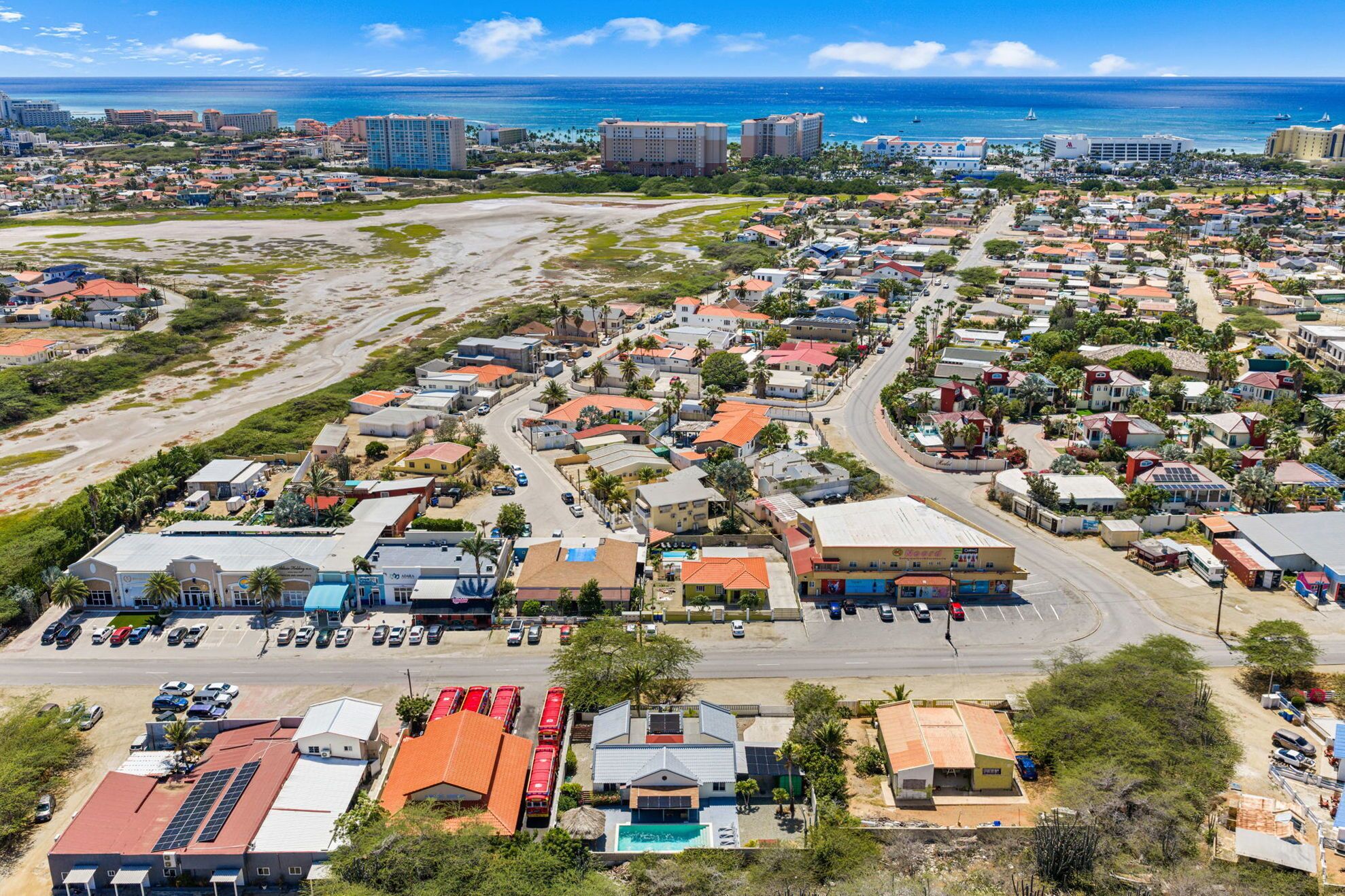 An aerial view of a coastal town with a mix of residential and commercial buildings, a beach, and a marina.
