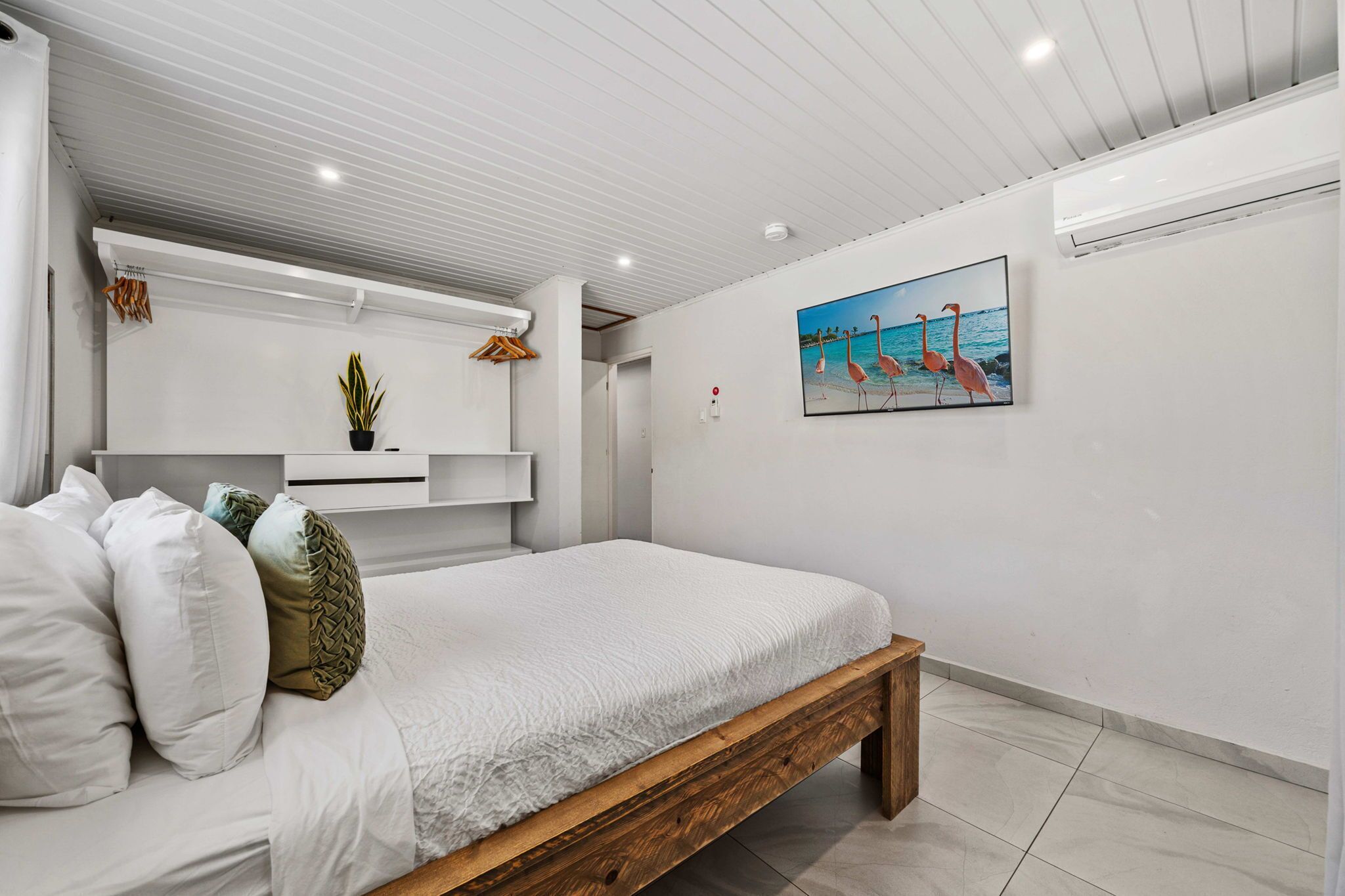 Un dormitorio con una cama de madera, ropa de cama blanca, una planta en maceta y un cuadro de flamencos en la pared.