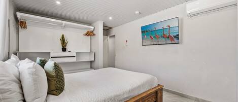 Un dormitorio con una cama de madera, ropa de cama blanca, una planta en maceta y un cuadro de flamencos en la pared.