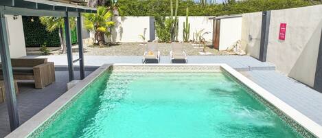 Ein rechteckiger Pool mit klarem, türkisblauem Wasser, umgeben von einer weißen Mauer und einer Pergola mit Holzbanken.