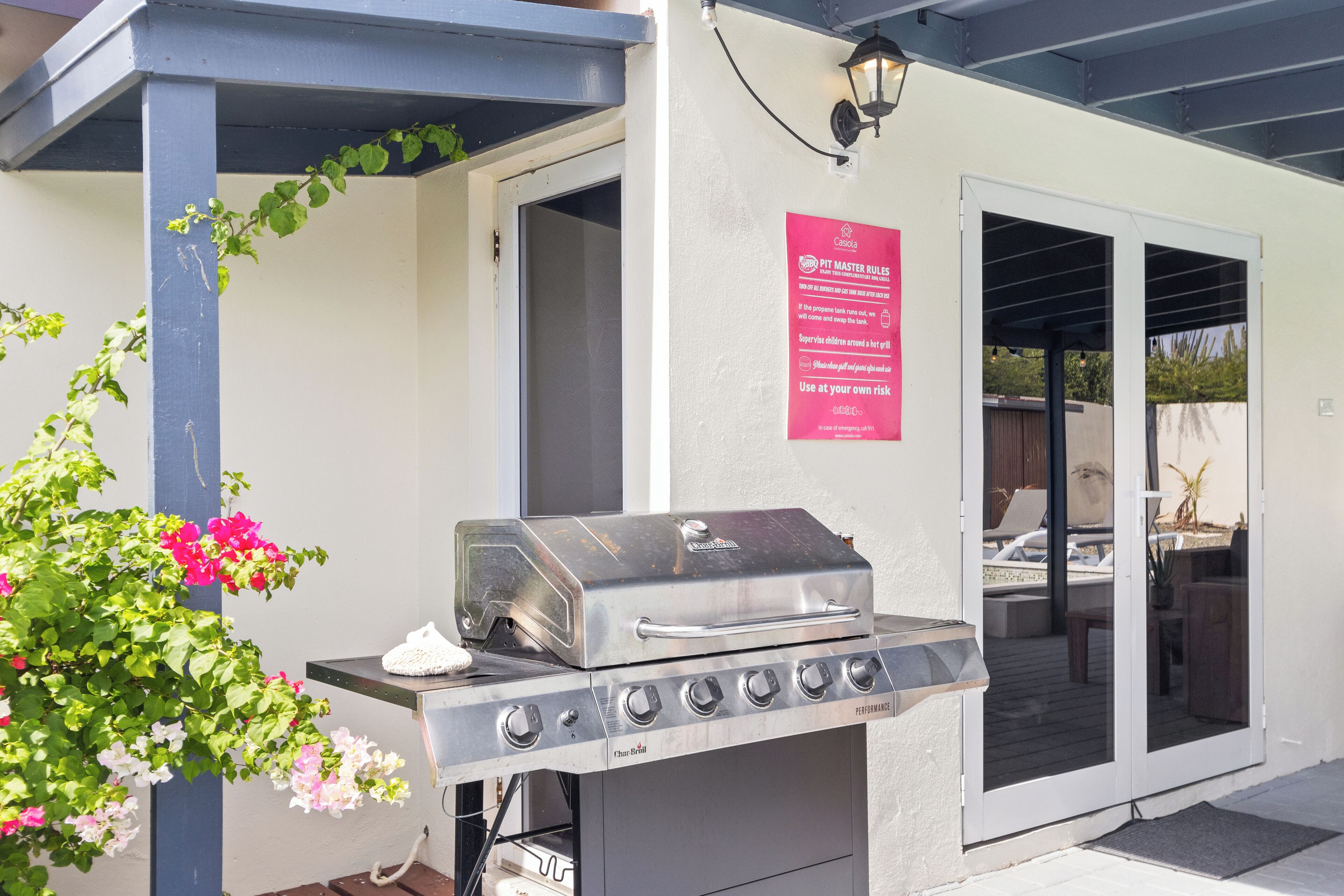 Un barbecue avec une finition en acier inoxydable, un panneau rouge affichant les règles à respecter pour le « pit master », et une vue sur un espace patio extérieur.