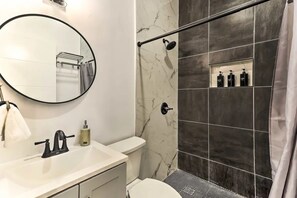 Ein modernes Badezimmer mit einem runden Spiegel, einem weißen Waschbecken, einer Toilette und einer Duschkabine mit dunklen Fliesen.