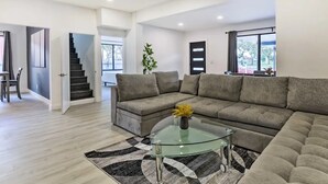 A modern living room with a sectional sofa, a glass coffee table, and a staircase leading to another room. - Spacious Miami Getaway ~ 8 Mi to South Beach! (Miami)