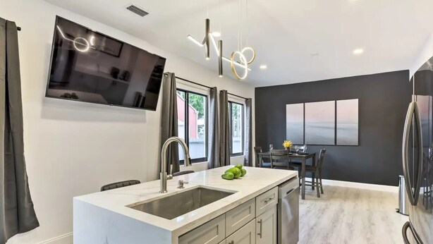 A modern kitchen with a large island, a built-in TV, and a dining area with a view. - Spacious Miami Getaway ~ 8 Mi to South Beach! (Miami)