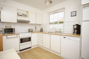 A modern kitchen with white cabinetry, a microwave, stove, oven, sink, and a coffee maker.