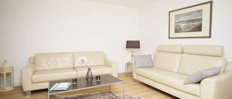 A living room with two cream-colored sofas, a glass coffee table, a lamp, and a framed picture on the wall.