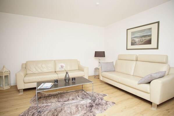 A living room with two cream-colored sofas, a glass coffee table, a lamp, and a framed picture on the wall.