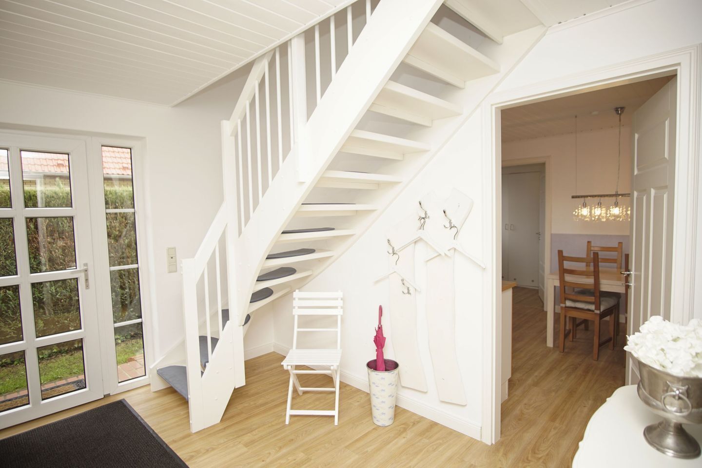 A staircase leading to an upper floor, a dining area with a chandelier, and a small table with a metal container.
