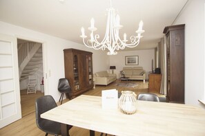 A spacious living room with a wooden dining table, a chandelier, a sofa, and a cabinet. - Wiking Vacation Home - Quiet location, beautiful house with a patio and garden (Binz)