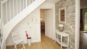A staircase with white railings, a wall-mounted coat rack, a small table with a flower vase, and a mirror on a stone-textured wall. - Vacation home Wiking - in a quiet location, beautiful vacation home with terrace and garden (Binz)