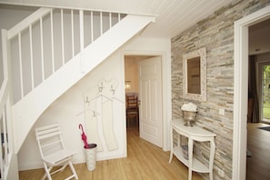 A staircase with white railings, a wall-mounted coat rack, a small table with a flower vase, and a mirror on a stone-textured wall.