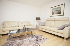 A modern living room with two cream-colored sofas, a glass coffee table, and a framed landscape painting on the wall. - Wiking Vacation Home - Quiet location, beautiful house with a patio and garden (Binz)