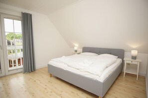 A bedroom with a large bed, two bedside tables with lamps, a sliding glass door, and a view of greenery outside. - Vacation home Wiking - in a quiet location, beautiful vacation home with terrace and garden (Binz)
