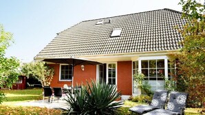 A two-story house with a tiled roof, a brick exterior, and a covered patio area with outdoor furniture. - Vacation home Wiking - in a quiet location, beautiful vacation home with terrace and garden (Binz)