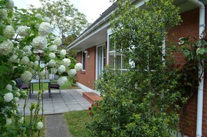 A brick house with a covered patio, a table and chairs, and a garden with white flowers. - Wiking Vacation Home - Quiet location, beautiful house with a patio and garden (Binz)