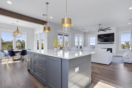 A modern kitchen with a large island, pendant lighting, and a dining area with blue chairs.