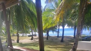 A wooden bench under a shaded area with a view of a beach and palm trees. - Anajawan Island Beachfront Resort  (General Luna)