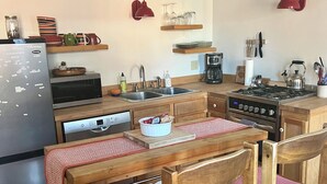 A compact kitchen with a refrigerator, microwave, sink, and a gas stove. There are wooden chairs with red cushions, a wooden table, and a small potted plant. - Belfast Beauty - Downtown Belfast (Belfast)