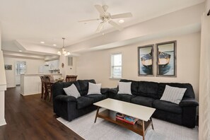 Sala de estar moderna com sofá preto, mesa de centro e área de jantar com cadeiras de madeira.