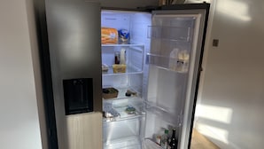 Un refrigerador moderno con varios estantes y compartimentos, incluyendo un cajón congelador, un cartón de leche y una botella de vino.