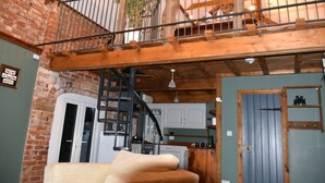 A rustic interior with exposed wooden beams, a brick wall, and a staircase leading to a loft area. - 2-Bed 18th Century Barn - Sleeps 6 - Pet Friendly (Boston)