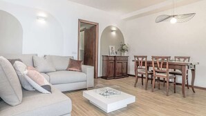 Un salon comprenant un canapé, une table basse, une table à manger avec des chaises, des meubles en bois et un luminaire suspendu.