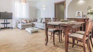 Un salon moderne avec une table à manger en bois, des chaises rembourrées, un canapé et un téléviseur à écran plat.