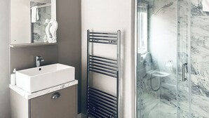 A bathroom with a sink, mirror, towel rack, and a glass shower enclosure.