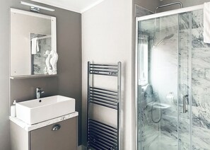 A bathroom with a sink, mirror, towel rack, and a glass shower enclosure.