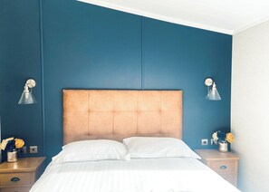 A bedroom with a tufted headboard, white bedding, two bedside tables with lamps, and a vase with flowers on one table.