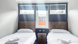 A twin room with two beds, a nightstand, and a window with blinds.