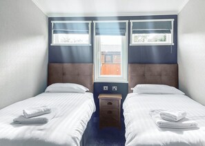 A twin room with two beds, a nightstand, and a window with blinds.