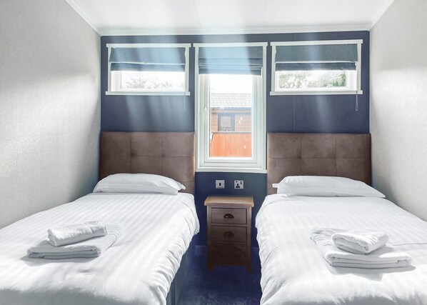 A twin room with two beds, a nightstand, and a window with blinds.