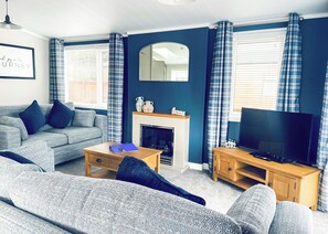 A living room with a sofa, a coffee table, a fireplace, a television, and curtains.