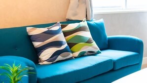 A blue sofa with two patterned cushions and a small green plant on the floor. - SHATOREYOYOGI401 (Tokyo)