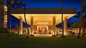A hotel entrance with a large central archway, palm trees, and a well-lit facade. - Kauai | Kauai Beach Escape | Pool & Beach (Kauai)