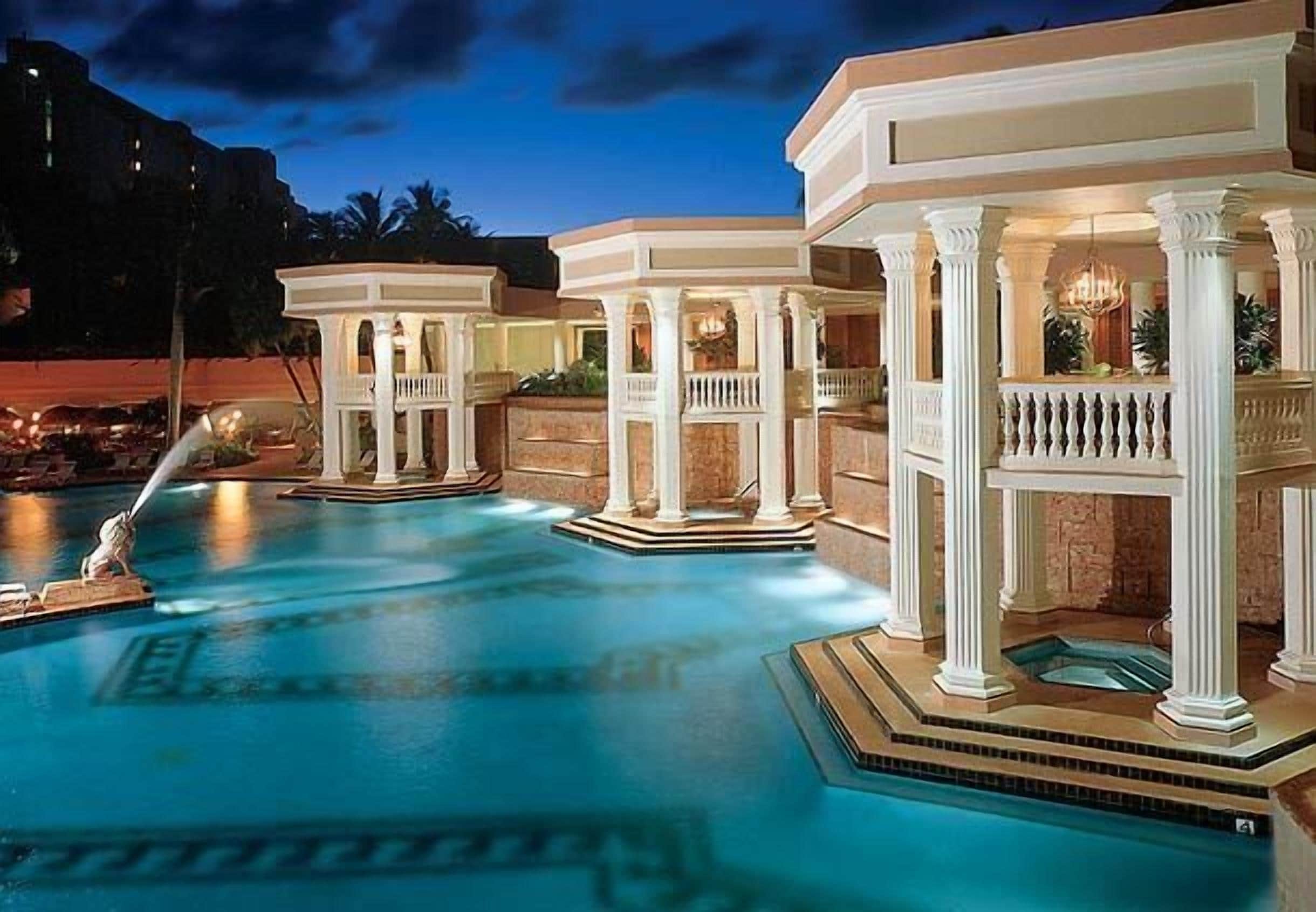 A swimming pool with multiple structures, including a gazebo and a hot tub area, surrounded by a landscaped garden.