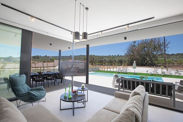 A modern living room with a large TV, comfortable seating, and a pool view.