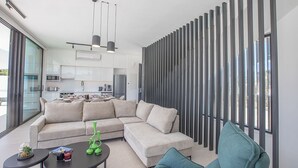 A modern living room with a sectional sofa, a small coffee table, and a dining area with a kitchen in the background. - Protaras Elite Pearl Villa EP14 -  a villa that sleeps 11 guests  in 5 bedrooms (Protaras)
