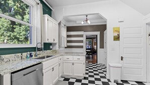 Cozinha com armários brancos, bancada de granito e chão quadriculado em preto e branco.