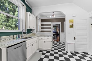 A kitchen with white cabinets, a granite countertop, and a black and white checkered floor. - Art House Apt 1 Northend Historic Apartment (Boise)