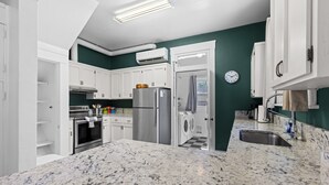Cozinha moderna com armários brancos, geladeira de aço inoxidável, forno embutido e bancada de granito.