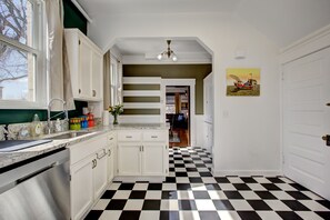 A kitchen with white cabinets, a black and white checkered floor, and a window with beige curtains.
