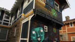 Une maison à deux étages dont la façade est ornée d’une fresque murale originale représentant un visage.